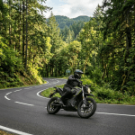 Motorcyclist wearing helmet and gear riding on curved road through dense green forest